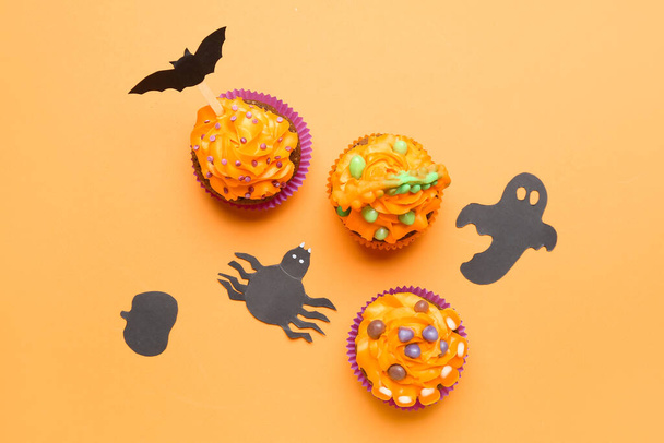 Tasty Halloween cupcakes with paper decor on orange background - Foto, afbeelding