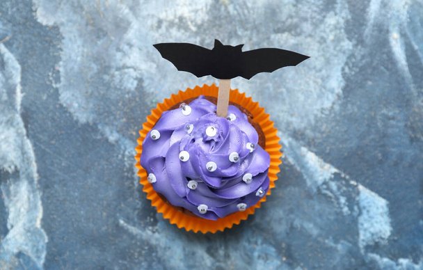 Leckere Halloween-Cupcake mit Papierfledermaus auf Grunge-Hintergrund - Foto, Bild
