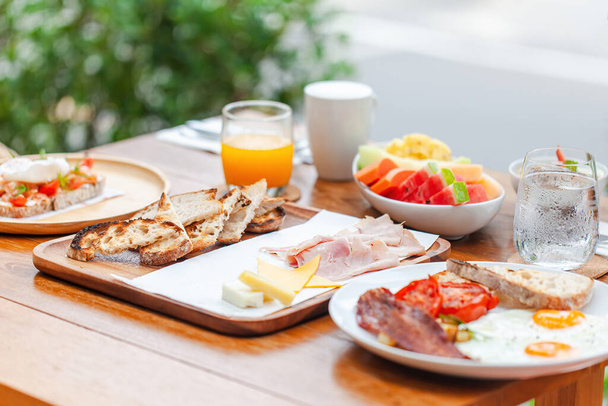 Healthy breakfast with eggs, bacon and ham in outdoors hotel cafe. Lunch served with orange juice, toast, cheese and fruits. Balanced diet. - Фото, изображение