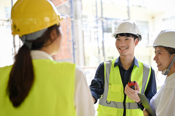 Mutlu ve neşeli genç Asyalı inşaat mühendisi inşaat müfettişi ve mimarıyla şantiyede harika bir konuşma yapıyor.. - Fotoğraf, Görsel