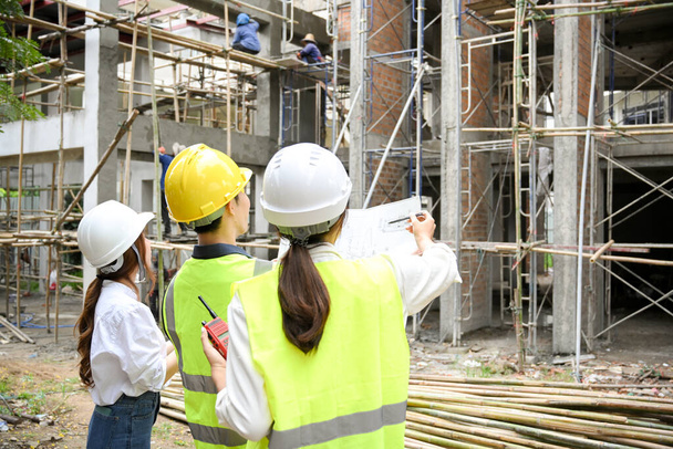 Eine Gruppe von Ingenieuren, Architekten oder Bauinspektoren in Schutzhelm und Uniform steht gemeinsam vor der Baustelle. - Foto, Bild