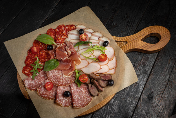 salami with sausage, ham, tomatoes, olives and basil on wooden board - Photo, image