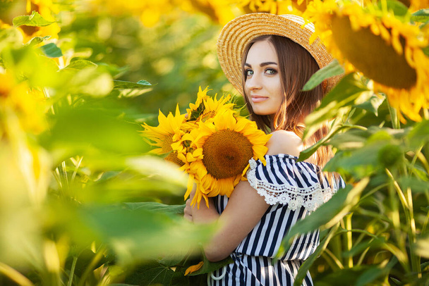 Bela jovem encaracolado em um campo de girassol com um chapéu de vime. - Foto, Imagem
