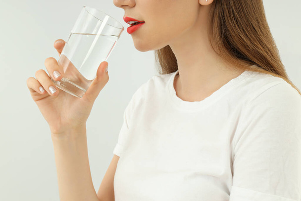 Jeune femme boire de l'eau du verre sur fond clair - Photo, image