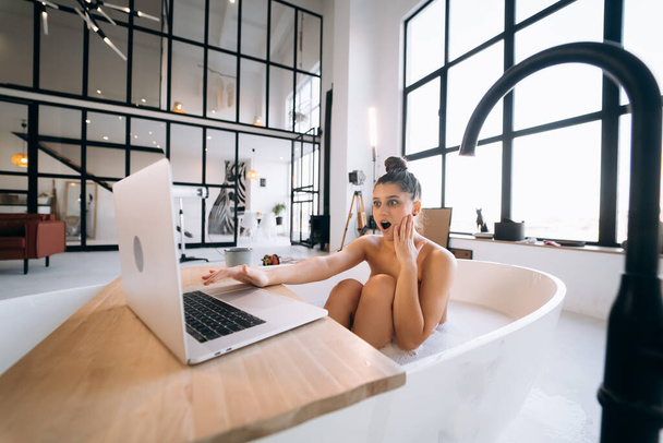 Jovem mulher trabalhando no laptop enquanto toma uma banheira em casa - Foto, Imagem