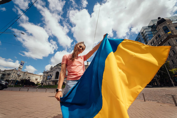 Ukrayna bayrağı taşıyan genç bir kadın şehirde yürüyor. - Fotoğraf, Görsel
