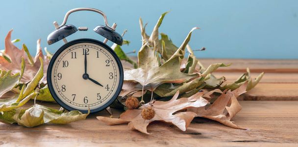 Переход на летнее и зимнее время. Черный будильник и осенние листья на деревянном столе, копия спака - Фото, изображение