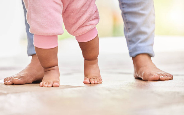 Low Cropped Nahaufnahme einer gemischten Rasse unkenntlich Mutter und kleinen Töchtern Füße stehen auf dem Boden zusammen zu Hause. kleines Baby mit kleinen süßen Zehen, das mit seiner Mutter laufen lernt. Die Anleihe wird. - Foto, Bild