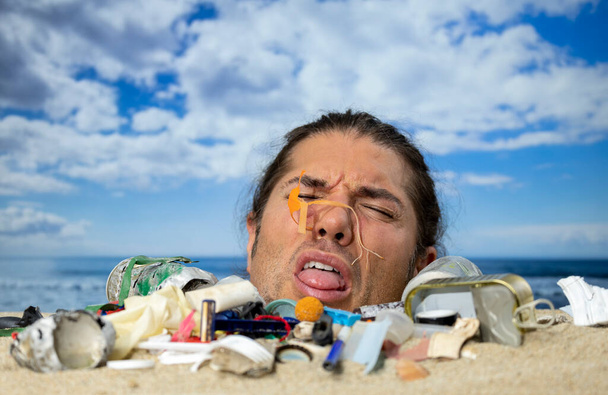 Mężczyzna zakopany po uszy na plaży pokryty śmieciami i odpadami z tworzyw sztucznych.  - Zdjęcie, obraz