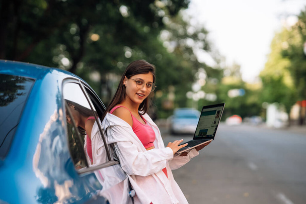 Eine junge Frau benutzt einen Laptop in der Nähe eines Autos in der Innenstadt - Foto, Bild