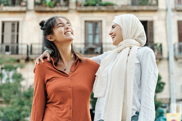 Amigos femeninos multiétnicos abrazándose y sonriendo mientras se divierten juntos al aire libre en la calle. Concepto de amistad. - Foto, Imagen
