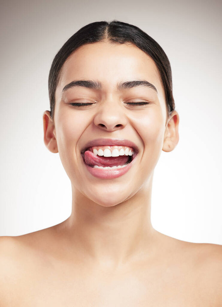 Young joyful mixed race woman sticking out her tongue and posing against a grey studio background. Confident hispanic female smiling while posing against a background. - Φωτογραφία, εικόνα