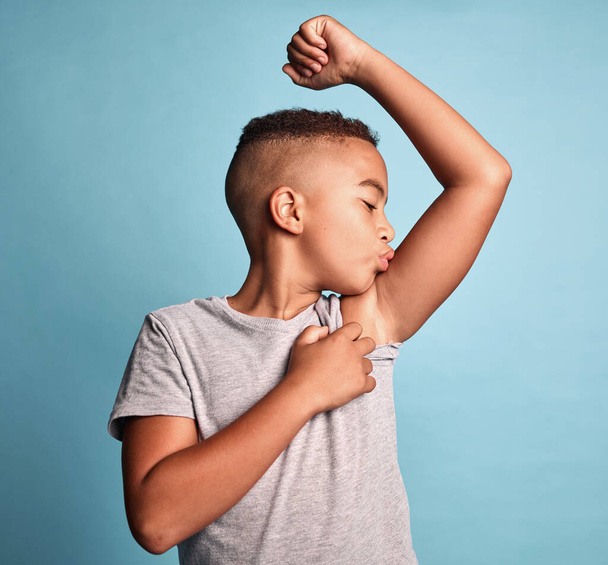Children, bicep and kiss with a boy bodybuilder in studio on a blue background for fitness, health or wellness. Sports, strong and kids with a young male child kissing his arm muscle during training. - Photo, Image