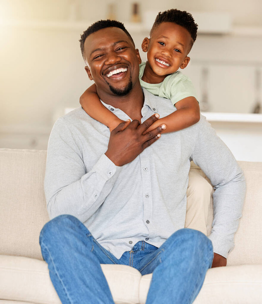 Porträt eines liebevollen schwarzen Mannes, der sein Kind auf einer Couch hält. Afroamerikanischer Vater, der zu Hause mit seinem Sohn zusammenlebt. Schwarzer Single-Papa lacht und hat Spaß mit seinem glücklichen Jungen auf einem Sofa. - Foto, Bild