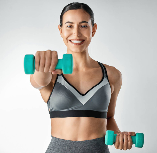 Crushing her workout with just a pair of dumbbells. Studio portrait of a sporty young woman exercising with dumbbells against a grey a background - Φωτογραφία, εικόνα