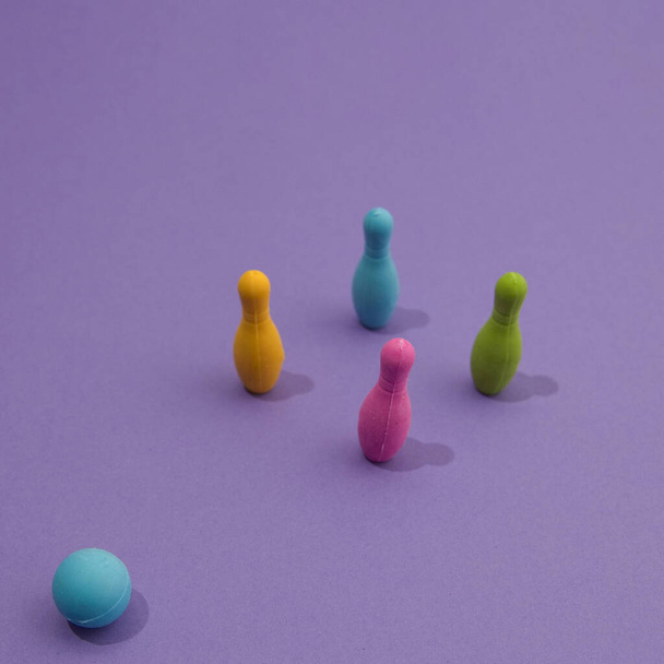 Beautiful shot of colorful bowling pins with a blue ball on the purple background with shadow. Playground minimalistic scene. - Zdjęcie, obraz