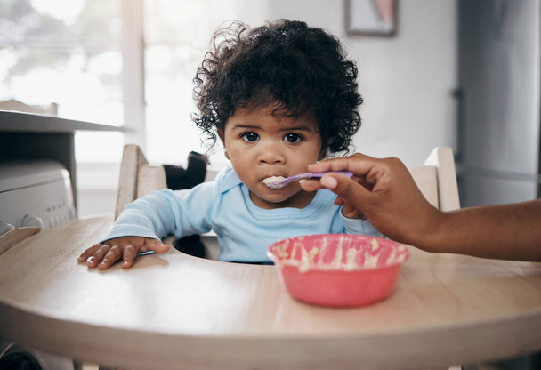 She doesnt enjoy eating breakfast. an adorable little girl sitting in the kitchen and being fed by her mother - Foto, Imagen
