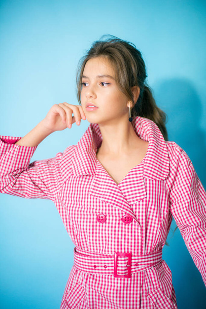 A cute teenage girl with long dark hair in a trendy red-plaid raincoat on a blue background in the studio. beauty and fashion - Foto, afbeelding
