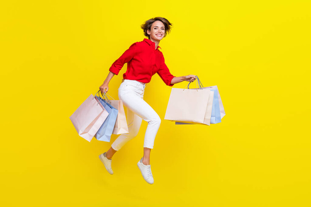 Full size photo of energetic girl hold packages jump hurry rush isolated on yellow color background. - Photo, Image