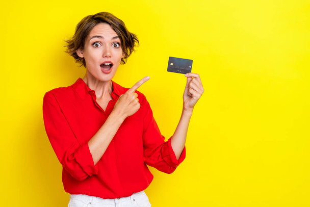 Closeup photo of young beautiful girlish lady wear stylish bright red shirt excited finger point new card pay salary shock isolated on yellow color background. - Фото, зображення