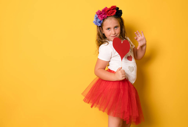 Photo of charming young child girl party clothes holding big red paper heart isolated yellow color background - Фото, зображення