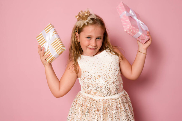 Picture of happy little girl child standing isolated over pink background. Looking camera holding gift box surprise. - Photo, Image