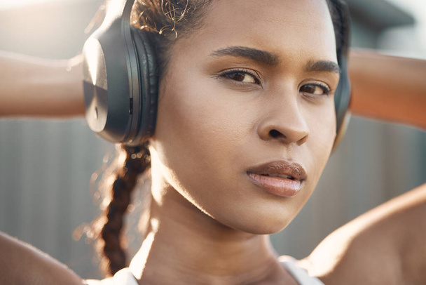 Closeup portrait of one fit young hispanic woman listening to music with headphones while exercising in an urban setting outdoors. Face of focused and motivated female athlete ready for training work. - Photo, image
