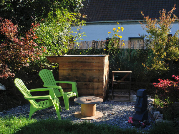 リラックスした植物環境の中で、三角形の木製のスパ、 2つの緑の椅子と小さな丸いテーブルからなる庭のリラクゼーションスペース。. - 写真・画像