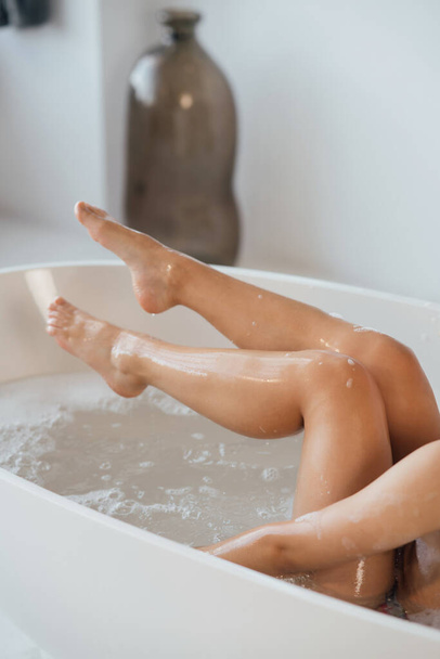 Cropped view of young woman lying in foamy bath, demonstrating silky skin on her legs - Foto, Bild