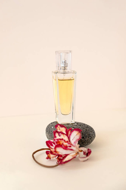 Состав желтой парфюмерной бутылки, балансирующей на гальке черного цвета и сухом цветке тюльпана на бежевом фоне. - Фото, изображение