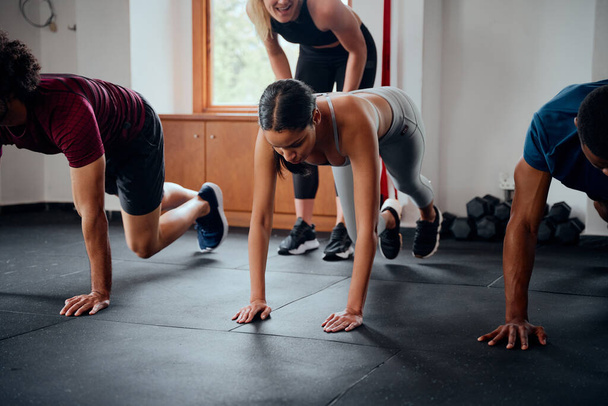 Group of determined multiracial young adults in sportswear with trainer doing mountain climbers at the gym - Zdjęcie, obraz