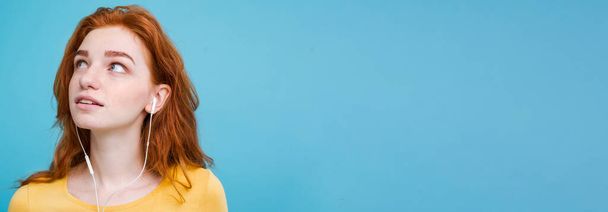 Lifestyle concept - Портрет веселой жизнерадостной рыжеволосой девушки с имбирными волосами, которая любит слушать музыку в наушниках и радостно улыбается камере. Изолирован на фоне Blue Pastel. Копирование пространства
. - Фото, изображение