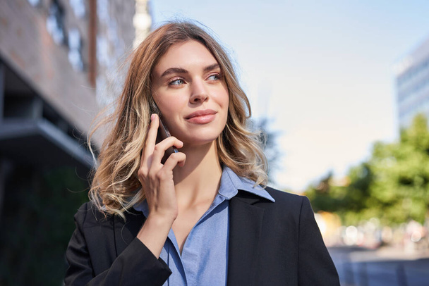Close-up portret van lachende verkoopster, succesvolle vrouwelijke manager met telefoongesprek, telefoon opnemen en lopen op straat. - Foto, afbeelding