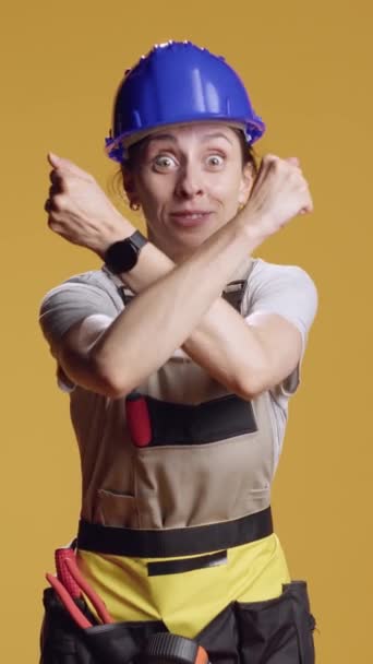 Verticale video: Portret van een sterke klusjesvrouw met gekruiste armen, reclame stop en breek gebaar over gele achtergrond. Constructor met timeout en afwerking symbool in de studio. - Video