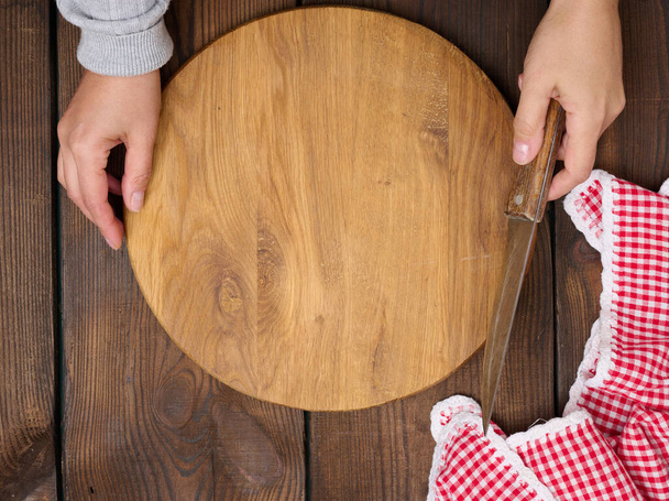 Two female hands hold a round empty wooden board on a brown table, top view - Photo, Image