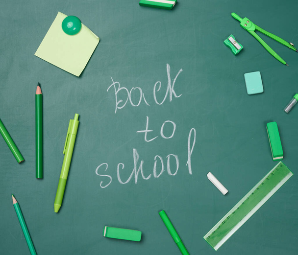 School supplies on empty green chalk board, top view. Chalk lettering back to school - Photo, Image