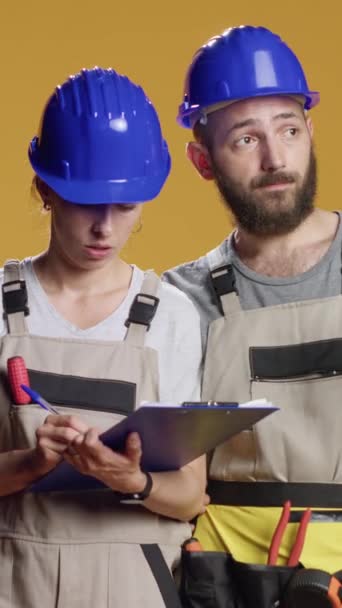 Vídeo vertical: Trabajadores de la construcción calculando la medición en papeles, tomando notas y planificando el proceso de construcción. El uso de cascos y monos para trabajar en la renovación y renovación, industrial - Metraje, vídeo