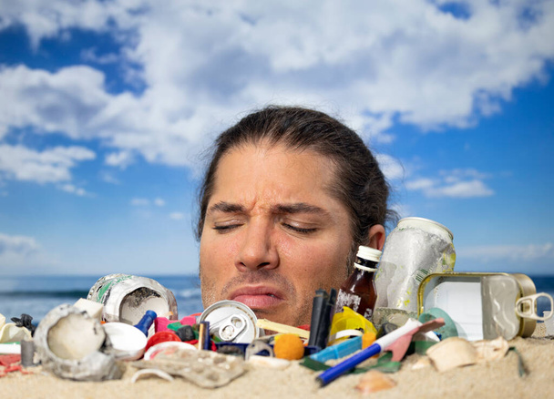 Un hombre enterrado hasta la cabeza en una playa cubierta de basura y residuos plásticos - Foto, Imagen