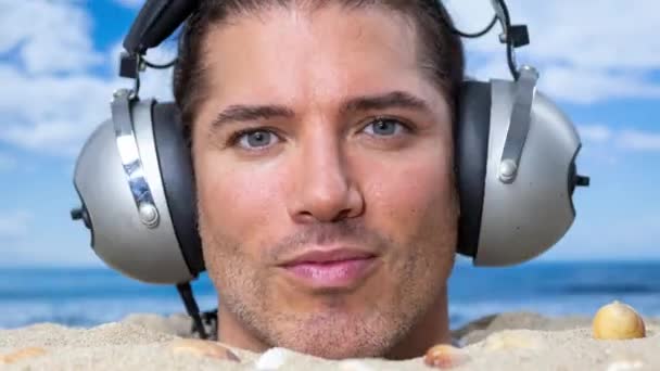 Un hombre enterrado en su cabeza en una playa escuchando música con auriculares cambiantes - Metraje, vídeo