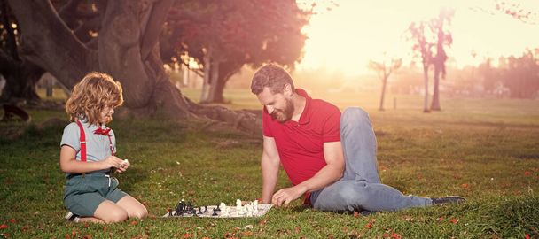 Banner van vader en kind spelen schaak logica spel. Vader en zoon schaken op gras in het park. Vaderdag. - Foto, afbeelding