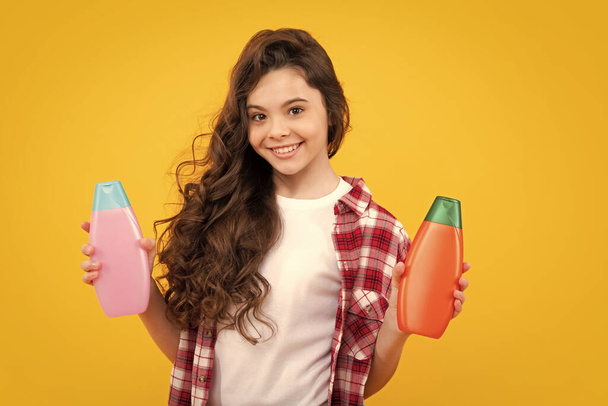 Child teen girl with shampoos conditioners and shower gel. Long hair care of teenager. Presenting cosmetic product, shampoo bottle. Happy teenager, positive and smiling emotions of teen girl - Photo, Image
