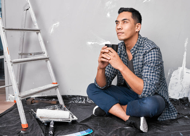 Çekici genç Asyalı bir adam yerde oturup DIY 'e kahve molası veriyor. Yüksek kalite fotoğraf - Fotoğraf, Görsel