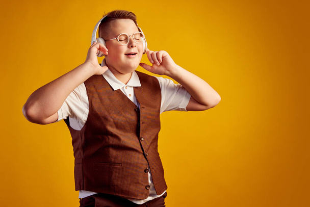 Happy smiling boy in retro costume listening to music in headphones isolated over orange color background. Vintage fashion, music, youth, emotions. Copy cpace for ad, text. - Photo, image