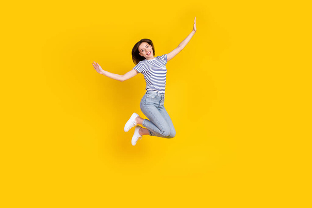 Full length photo of nice young girl spread hands plane jumping ad poster wear stylish striped garment isolated on yellow color background. - Foto, Bild