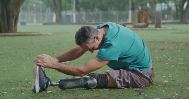 Un atleta discapacitado mayor de mediana edad motivado estirando la pierna protésica - Metraje, vídeo