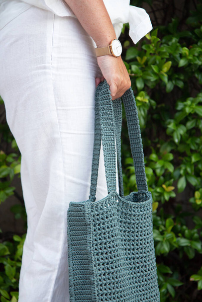 Woman holds a handmade blue knitted bag in her hand outdoors. Sustainable shopping. Wasteless lifestyle. Female with a jute bag with her own hands on a walk. Close up - Valokuva, kuva