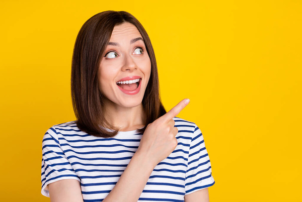 Portrait of cute gorgeous positive girl wear striped t-shirt directing empty space open mouth isolated on yellow color background. - 写真・画像
