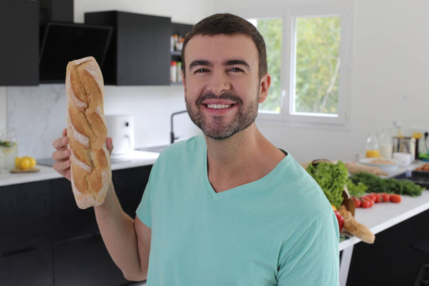 portrait of handsome young man holding freshly baked loaf of bread at home - Fotografie, Obrázek