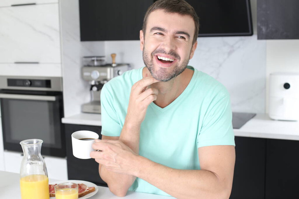 portrait of handsome young man with coffee and sandwiches for breakfast at home - Foto, afbeelding