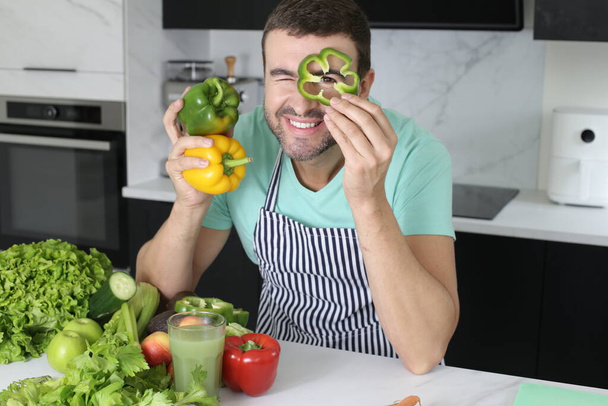 portrait of handsome young man playing with vegetables while cooking at home - Photo, Image
